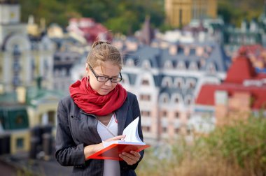 Ceket ve gözlük güzel ciddi kadın yaz binalar karşı kırmızı kitap okur