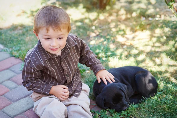 Kleine jongen speelt met een zwarte Labrador puppy — Stockfoto