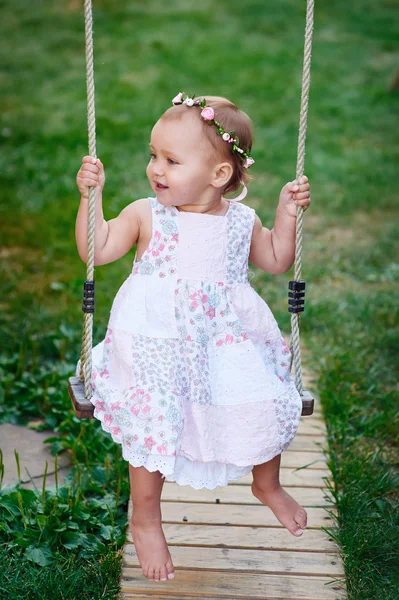 Schattige babymeisje genieten van een schommel rijden op een speelplaats in een park — Stockfoto