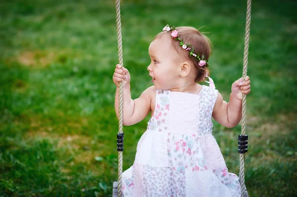 Очаровательная малышка наслаждается катанием на качелях на детской площадке в парке — стоковое фото
