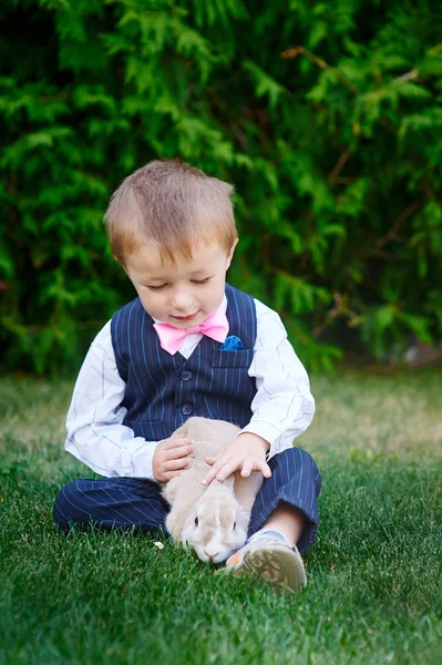 Kleiner Junge im Anzug spielt im Park mit einem Kaninchen — Stockfoto