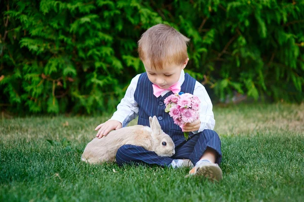 Liten pojke i kostym spela i parken med en kanin — Stockfoto