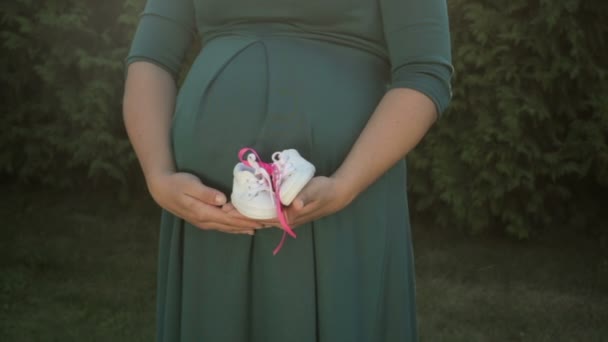 Изображение беременной женщины с маленькими детскими туфельками в руке — стоковое видео