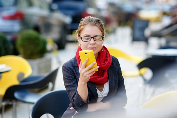 Bir kafede otururken ve seyir telefon içinde gözlüklü kadın — Stok fotoğraf