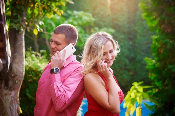 Homem e mulher em vestido vermelho falando ao telefone uns com os outros — Fotografia de Stock