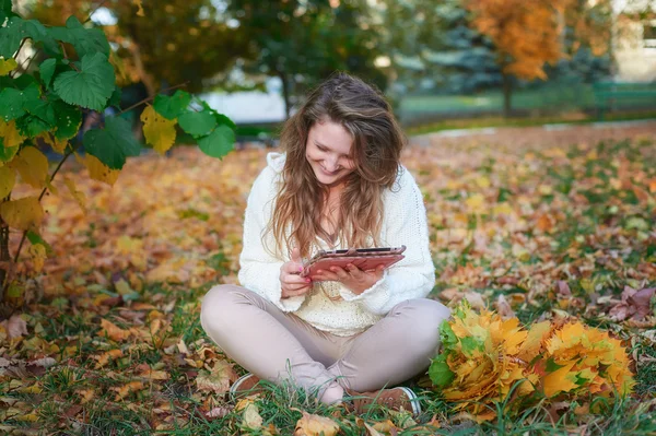 Schöne junge Frau mit Tablet sitzt im Herbstpark — Stockfoto