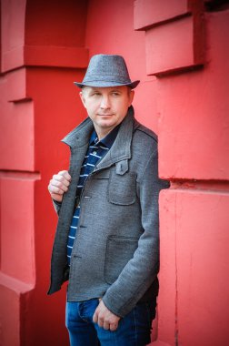 Kırmızı duvarın yanında şapkalı bir adam