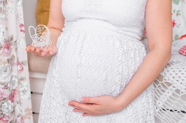 Mujer embarazada en un vestido blanco sosteniéndose para el estómago y cochecito pequeño — Foto de Stock