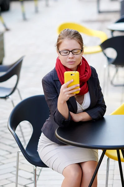 Mujer de negocios sentada en una mesa en un café y escribir SMS en el teléfono — Foto de Stock