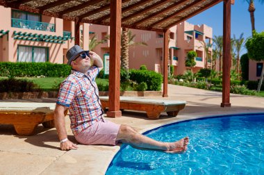 Havuzun kenarında oturan şapkalı mutlu adam