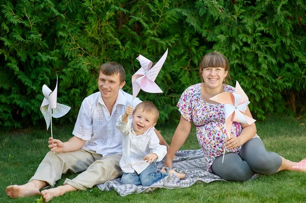 Mladá rodina sedí na trávě v parku s hračkami — Stock fotografie