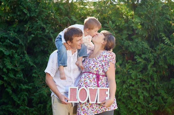 Family of mother father and boy, little boy kissing his mom and parents takes letters LOVE — Stock Photo, Image