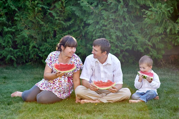 Père, mère et fils mangeant pastèque assis sur l'herbe — Photo