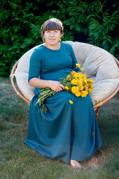 Pregnant woman sitting on a chair with a bouquet of flowers — Stock Photo, Image