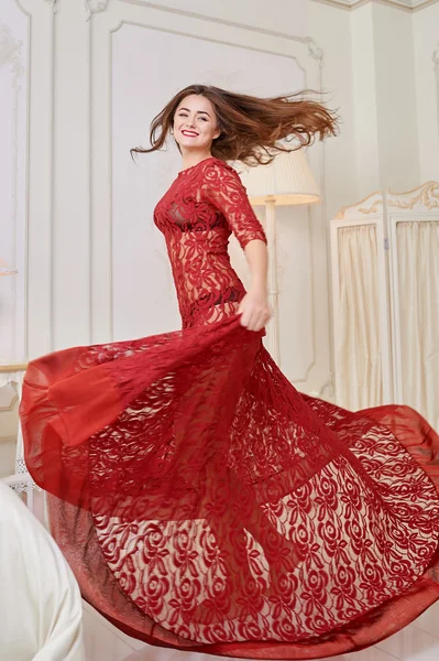 Happy woman in a red dress jumping out of bed — Stock Photo, Image