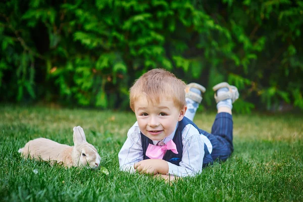 Kleiner Junge spielt mit einem Hasen im Sommergarten — Stockfoto