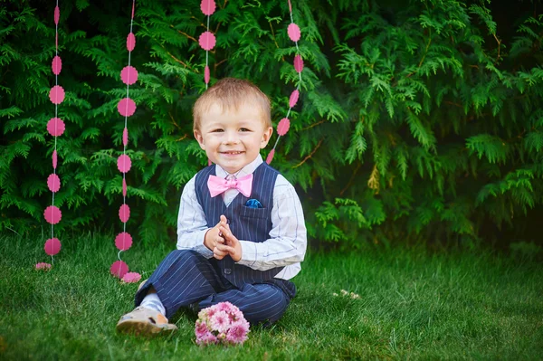 Glad liten pojke sitter i parken på gräset — Stockfoto