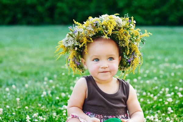 Kleines Mädchen mit Kranz auf dem Kopf auf dem Gras sitzend — Stockfoto