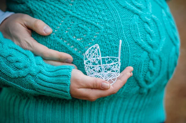 Concepto de embarazo: vientre con la mano sosteniendo un cochecito de juguete pequeño delante — Foto de Stock