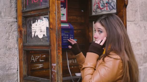 Красивая молодая женщина разговаривает по телефону в телефонной будке — стоковое видео