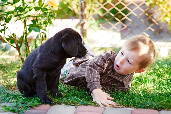 Chłopiec bawi się czarny szczeniak Labrador w ogrodzie — Zdjęcie stockowe