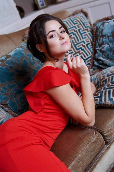 Beautiful woman in red dress relaxing on a sofa in luxury interior — Stock Photo, Image