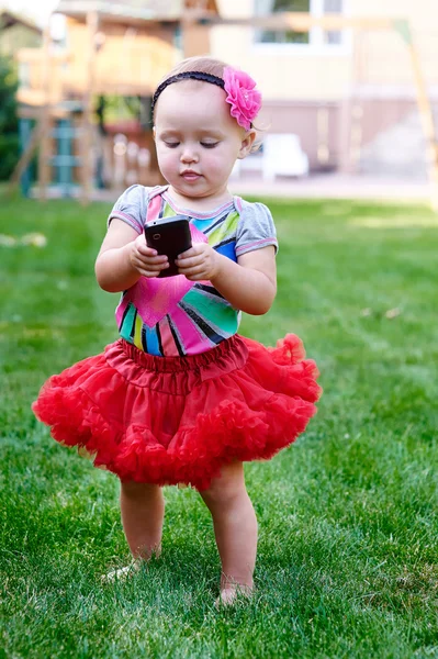 Little girl with a phone in a red skirt — Stock Photo, Image