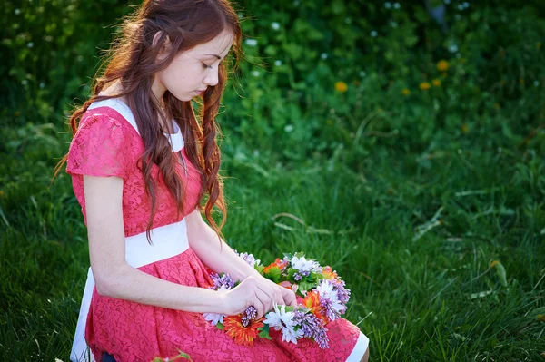 Beautiful woman weaves a wreath on the grass — Stock Photo, Image