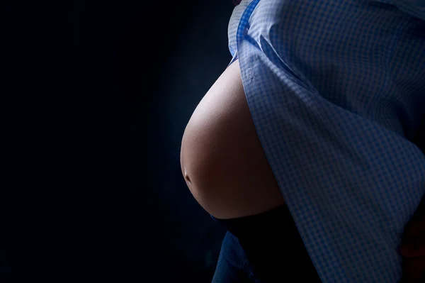 Buik van zwangere vrouw op een donkere achtergrond — Stockfoto