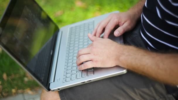 Junger Mann sitzt mit Laptop auf der Parkbank — Stockvideo