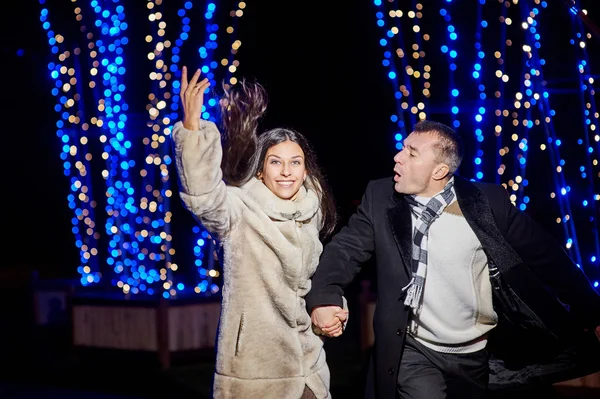 Счастливая молодая пара, бегущая в вечернем парке с освещением — стоковое фото