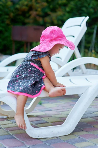 Bambina con un cappello rosso si siede su un lettino — Foto Stock