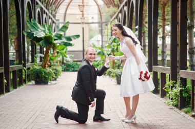 groom kneels on one knee in front of a happy bride