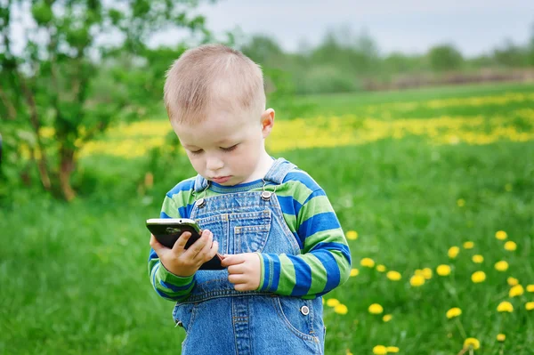 Little boy looking at a smartphone on a meadow — Stock Photo, Image