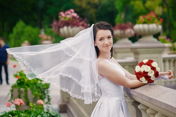 Emotional brunette bride in white dress posing at balcony near stone railing — Stock Photo, Image