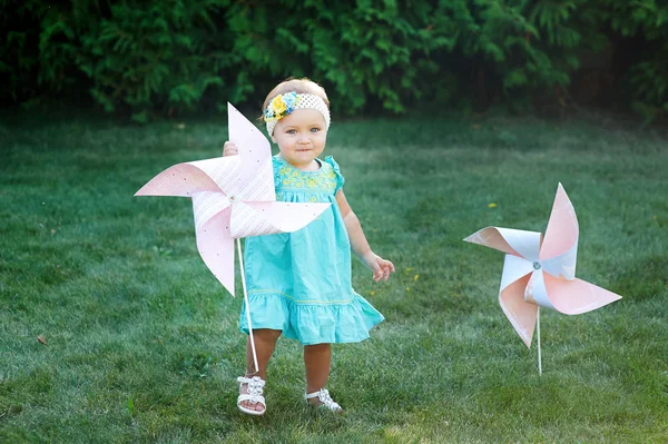 Счастливая улыбающаяся маленькая девочка, стоящая на лугу и держащая в руках игрушку белую ветряную мельницу — стоковое фото