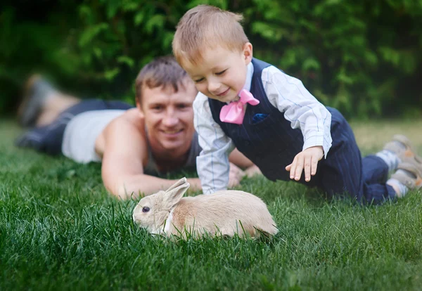 Kleine jongen met zijn vader spelen met een konijn op het gras — Stockfoto