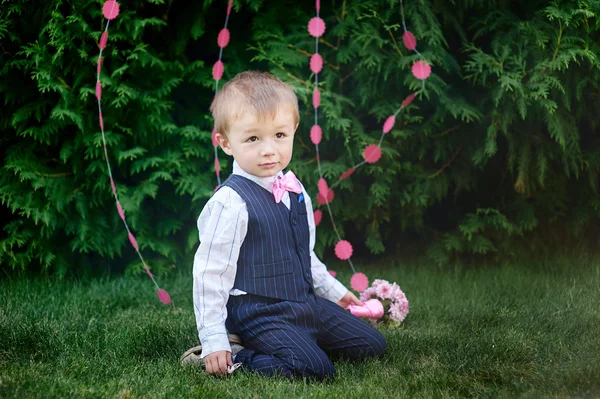 Petit garçon en costume avec un bouquet assis sur l'herbe — Photo