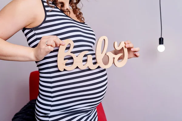 Barriga grávida com símbolo de texto bebê em suas mãos — Fotografia de Stock