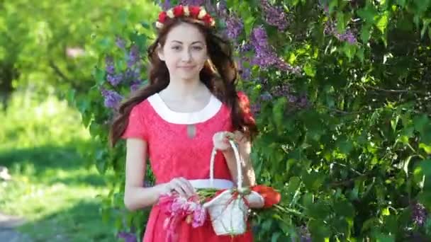 Schöne Frau in einem roten Kleid mit einem Kranz und einem Korb mit Tulpen — Stockvideo