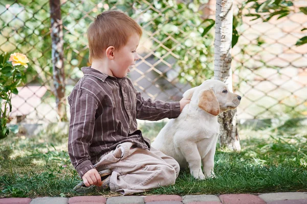 Bambino che gioca con un cucciolo di Labrador bianco — Foto Stock