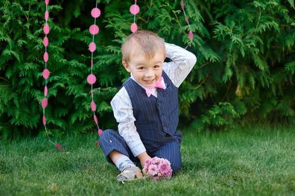 草の上に座って花束とスーツの小さな男の子 — ストック写真