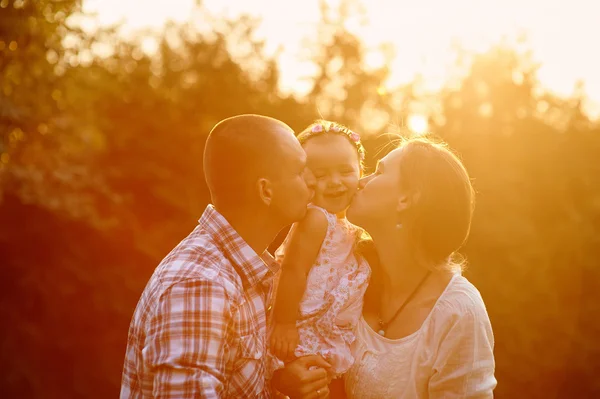 Felice famiglia mamma e papà tenendo la figlia tra le braccia e baciarla nel parco — Foto Stock