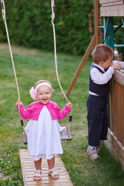 Маленькая девочка на детской площадке катается на качелях летом — стоковое фото
