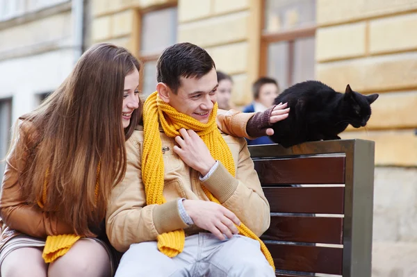 Glückliches junges Paar mit einer Katze auf einer Bank in der Stadt — Stockfoto