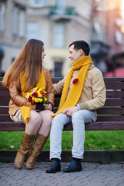 Love couple sitting on a bench with a bouquet of flowers — Stock Photo, Image