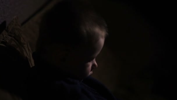 Μικρό αγόρι κάθεται στον καναπέ σε σκοτεινό δωμάτιο — Αρχείο Βίντεο
