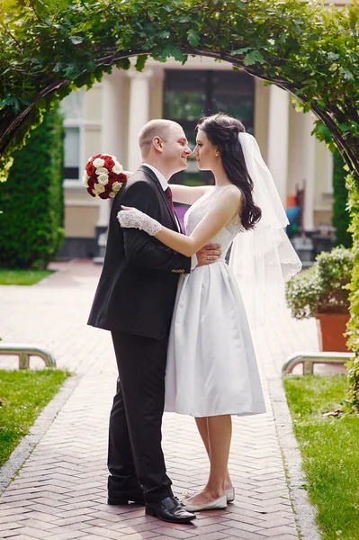 Bräutigam küsst seine Braut am Hochzeitstag in der Nähe von Bogen — Stockfoto
