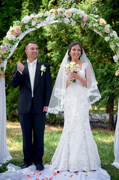 Noiva e noivo ficar perto do arco na cerimônia de casamento — Fotografia de Stock