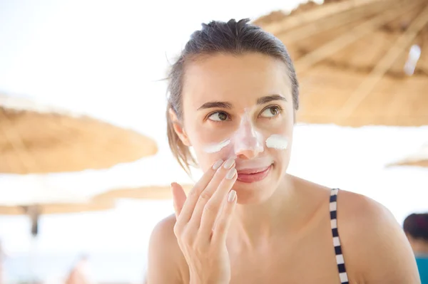 Beautiful woman smears face sunscreen at the beach for protection — Stock Photo, Image